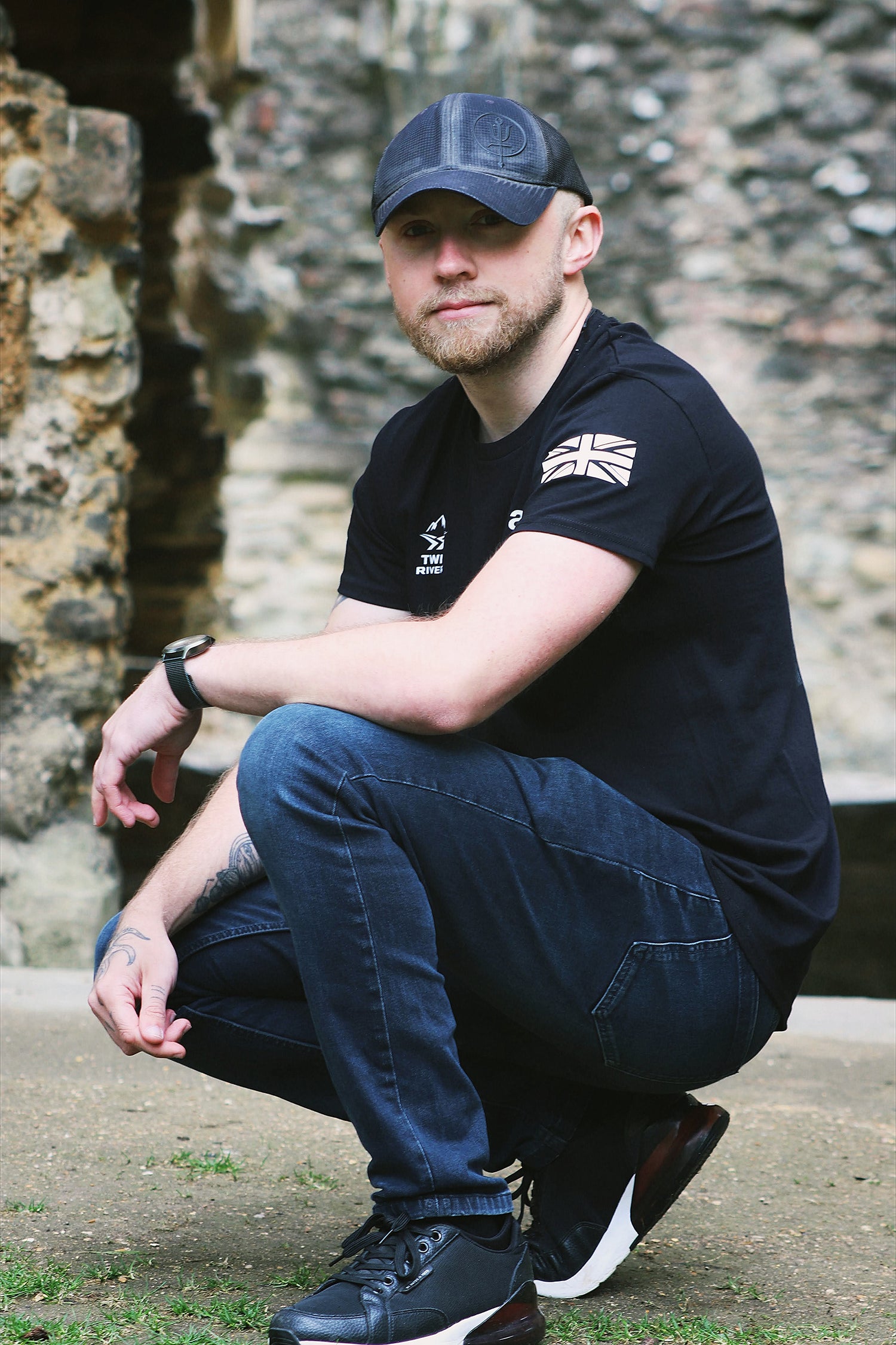 Man wearing a black t-shirt with a Union Jack design and blue jeans, sitting on stone steps.