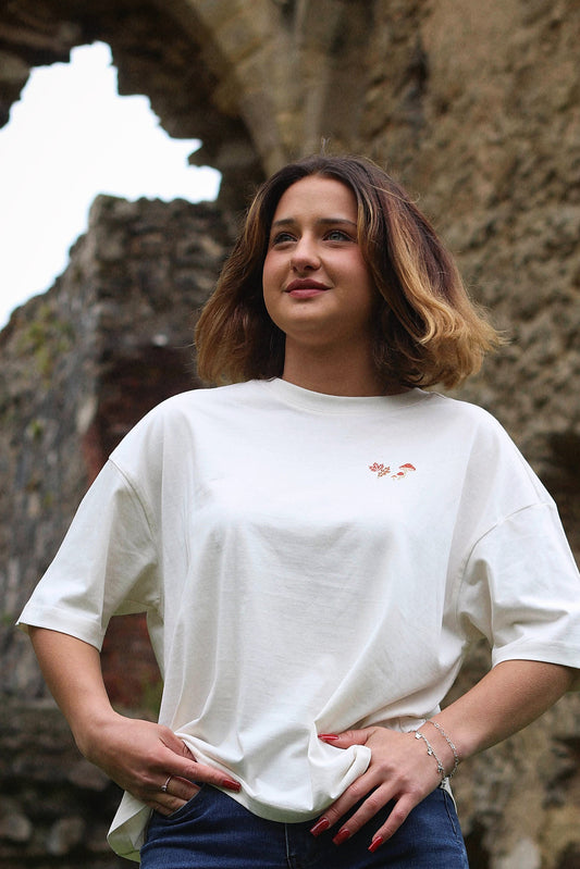 Woman wearing a white t-shirt with a small logo in front of stone ruins